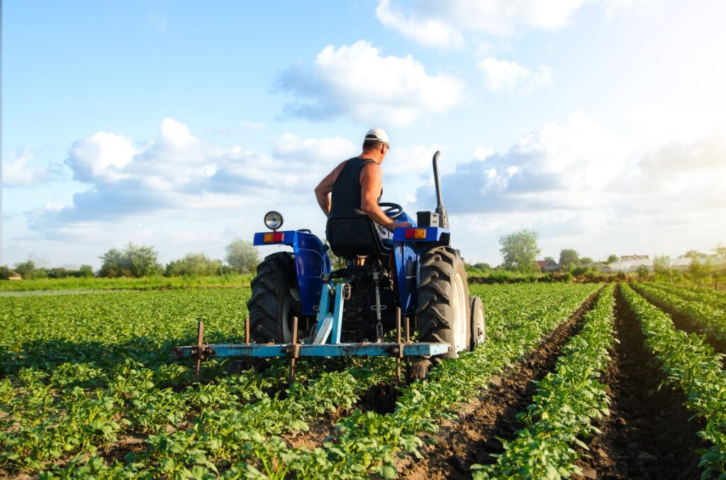 A farmer cultivating a field with a blue tractor, representing the careful planning needed for a successful business exit.